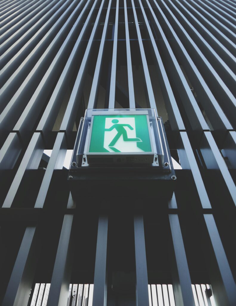 Vertical shot highlighting a green emergency exit sign on a modern building facade.