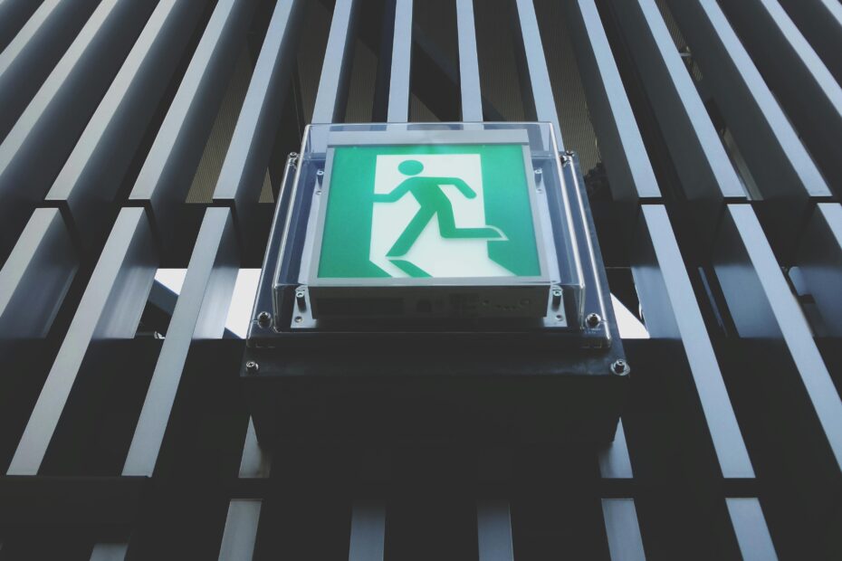 Vertical shot highlighting a green emergency exit sign on a modern building facade.