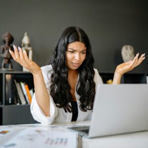 A frustrated businesswoman sits at her office desk, puzzled over her laptop.